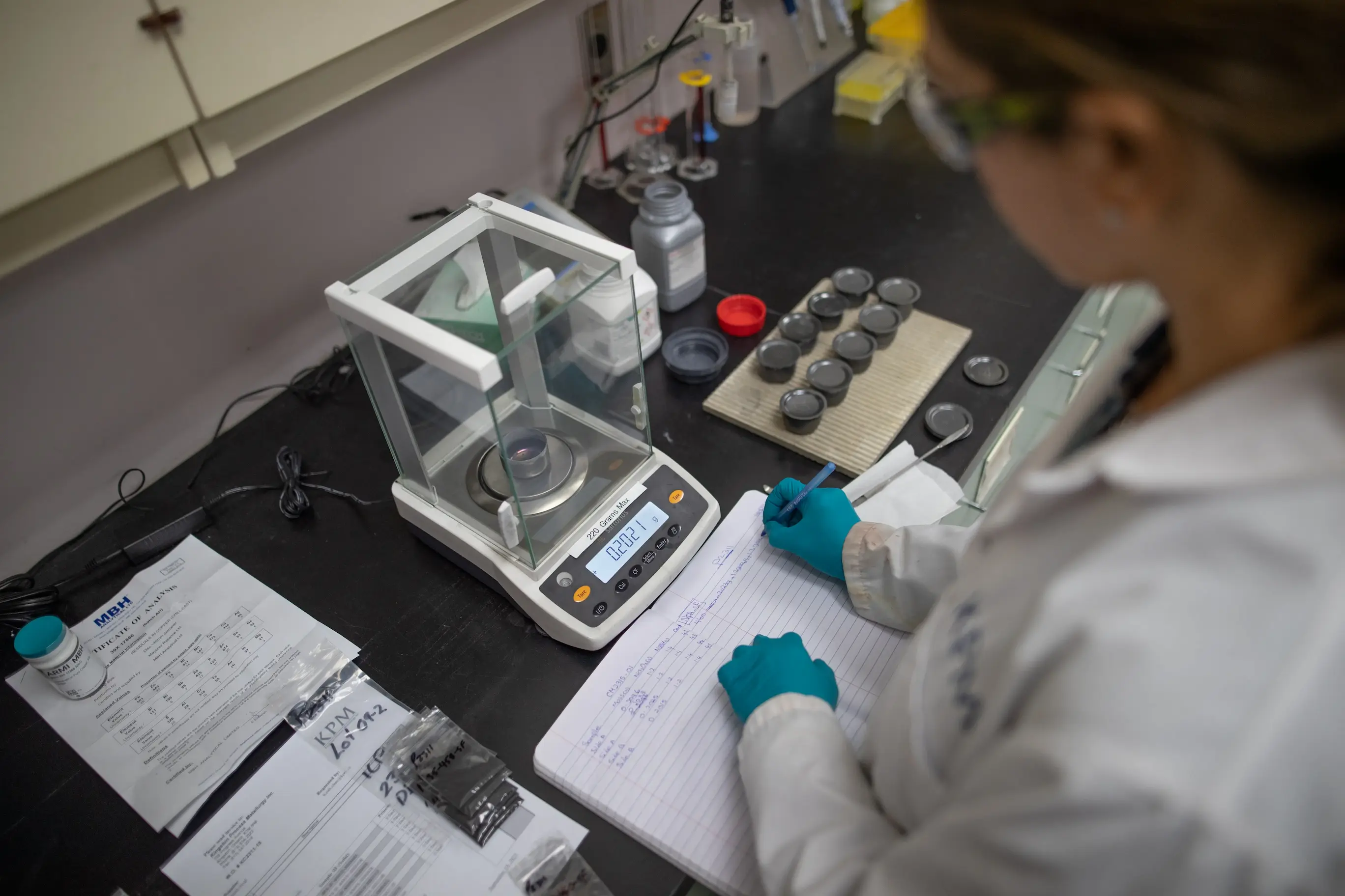 somebody recording data in a lab book from a scale